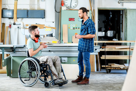 worker in wheelchair in a carpenter's workshop with his colleague in conversation