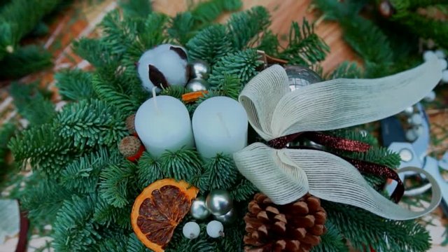 Christmas composition: pine tree branches, candles, christmas tree toys, bow, dry orange slices and cotton flower balls in a basket. Craft supply for handcrafted decorations on wooden table, close-up