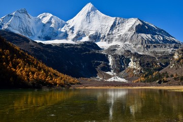 Sacred mountain Jambeyang (5,958m) with blue sky background and its reflection on icy clean lake. This place is supposed to be the real Shangrila. Daocheng Yading Nature Reserve, Sichuan, China. 