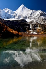 Sacred mountain Jambeyang (5,958m) with blue sky background and its reflection on icy clean lake. This place is supposed to be the real Shangrila. Daocheng Yading Nature Reserve, Sichuan, China. 