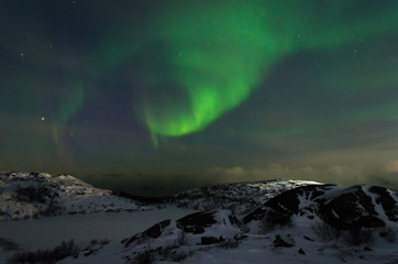 Fototapeta na wymiar Beautiful northern lights, aurora in the night sky above the snow-covered hills. Large stones and a frozen lake.