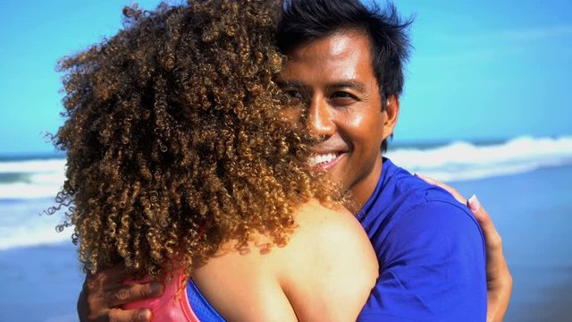Young loving smiling multi ethnic couple in colorful sportswear embracing on their beach vacation
