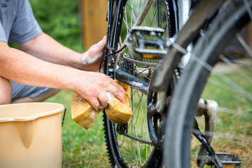 Man cleaning the bicycle by yellow sponge and preparation / product for washing - obrazy, fototapety, plakaty