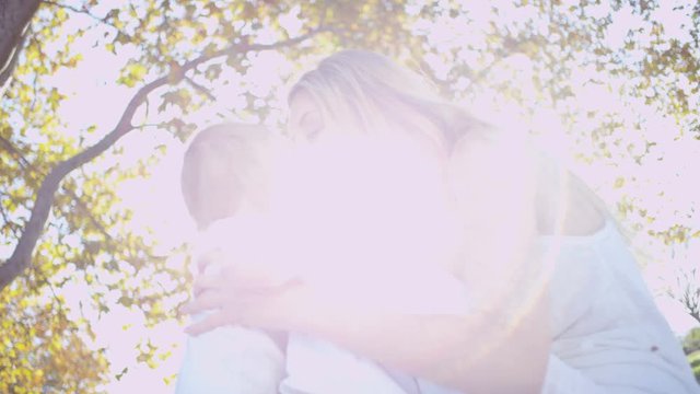 Attractive blonde Caucasian mother holding and kissing her baby boy in the sunshine outdoors 