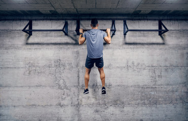Caucasian man doing pull-ups in the gym. Strive for progress and perfection.