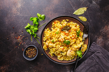 Rice with chicken in a black plate on a dark background, top view.