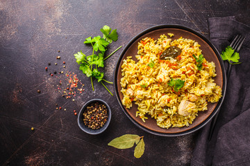 Rice with chicken in a black plate on a dark background, top view.