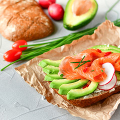 sandwich with avocado and salmon on a light background, green onions and gluten-free grain bread, radishes and tomatoes. concept diet food, copy space, sandwich take away, healthy fast food