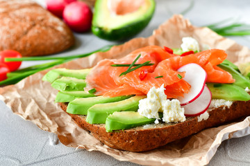 sandwich with avocado and salmon on a light background, green onions and gluten-free grain bread, radishes and tomatoes. concept diet food, copy space, sandwich take away, healthy fast food