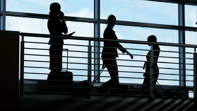 Silhouette of Asian American businesswoman using smartphone technology in airport building atrium with multi ethnic business travellers 