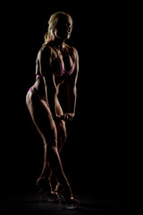 Athletic woman in pink bikini posing in studio. Attractive fitness lady with long blond hair showing her muscles