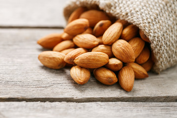 Almond nuts in a burlap bag on a wooden gray background.
