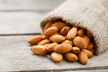 Almond nuts in a burlap bag on a wooden gray background.