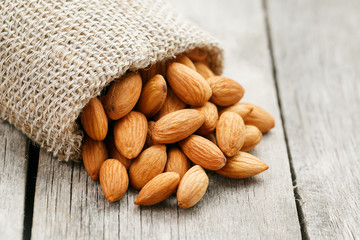 Almond nuts in a burlap bag on a wooden gray background.