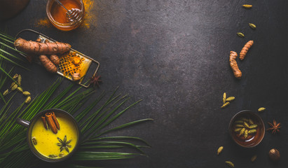 Golden turmeric milk with spices. Dark background frame with ingredients and palm leaves. Healthy...