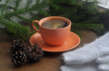 Obraz na płótnie Canvas A cup of hot coffee, fir branches, cones and handmade mittens tepdye near the winter window. Christmas and New Year.