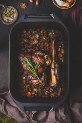 Slow cooked venison roast in black cast iron pan, top view. Braised leg of deer with bone and...