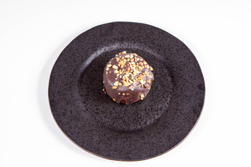 Rum ball decorated with chocolate and nuts on a black plate on a white background