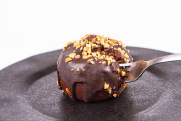 Rum ball decorated with chocolate and nuts on a black plate eaten with a fork on a white background