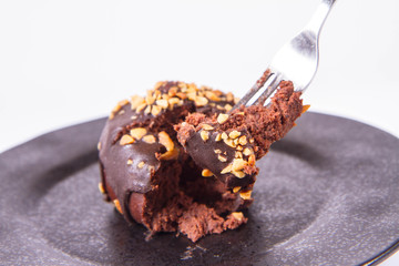 Rum ball decorated with chocolate and nuts on a black plate eaten with a fork on a white background