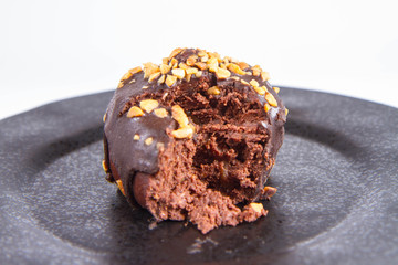 Rum ball decorated with chocolate and nuts on a black plate, partially eaten, on a white background