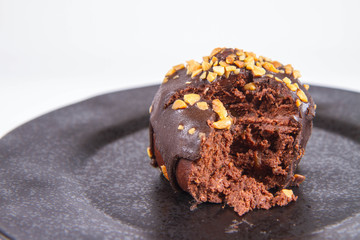 Rum ball decorated with chocolate and nuts on a black plate, partially eaten, on a white background
