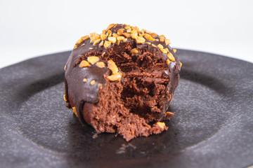 Rum ball decorated with chocolate and nuts on a black plate, partially eaten, on a white background