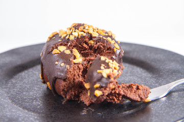Rum ball decorated with chocolate and nuts on a black plate eaten with a fork on a white background