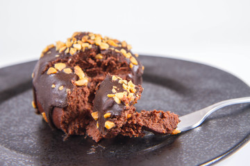 Rum ball decorated with chocolate and nuts on a black plate eaten with a fork on a white background