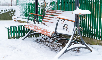 The wooden bench is all covered with snow