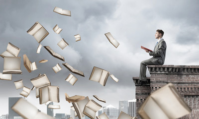 Man on roof reading book and many of them flying in air