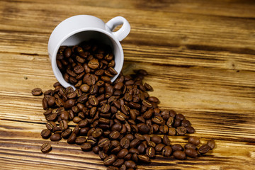 Roasted coffee beans spill out of cup on wooden table