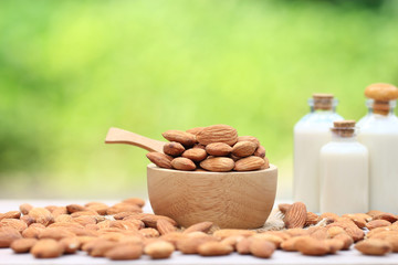 Almond in a bowl and almond milk in glass bottle on the table blurred natural green background with copy space