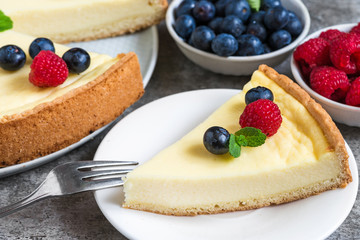 slice of New York cheesecake with fresh berries and mint with fork on stone background. close up