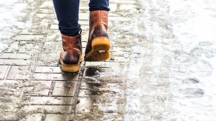 Naklejka premium Walk on wet melted ice pavement. Back view on the feet of a man walking along the icy pavement. Pair of shoe on icy road in winter. Abstract empty blank winter weather background