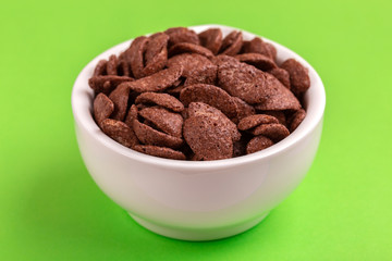 Crunchy chocolate corn flakes in bowl on bright green background
