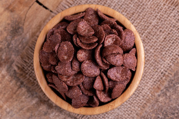 Crunchy chocolate corn flakes in wooden bowl with burlap napkin