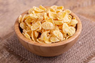 Crunchy corn flakes in wooden bowl with burlap napkin