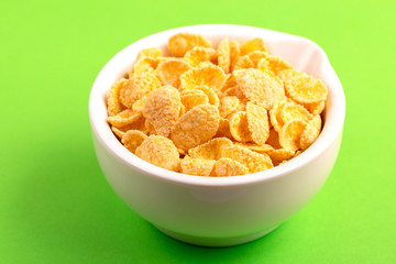 Crispy corn flakes in clay bowl on bright green background