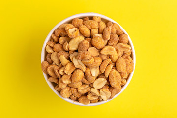 Roasted peanuts in paper cup on bright yellow background.