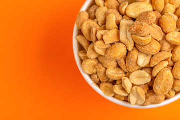 Roasted peanuts in paper cup on bright orange background