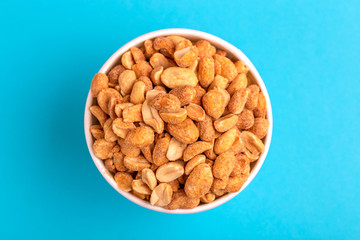 Roasted peanuts in paper cup on bright blue background
