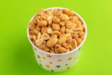 Roasted peanuts in paper cup on bright green background