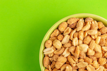 Roasted peanuts in bowl on bright green background