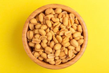 Roasted peanuts in wooden bowl on bright yellow background