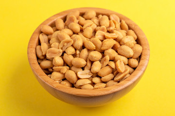 Roasted peanuts in wooden bowl on bright yellow background