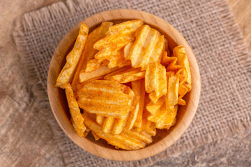 Crispy corrugated potato chips in wooden bowl on burlap napkin