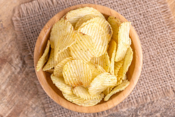 Crunchy corrugated potato chips in wooden bowl on burlap napkin