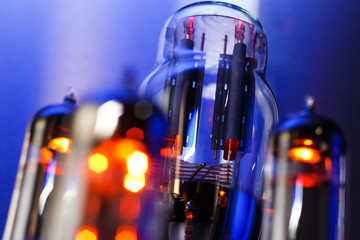 Vacuum electronic radio tube close-up. Glowing orange on dark blue background.