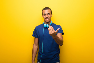 African american man with blue t-shirt on yellow background inviting to come with hand. Happy that you came